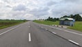 At the public transportation stop, a metal weather protection with a plastic canopy is installed on an asphalt road with markings.