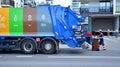 A public utility worker collects garbage from garbage cans in a garbage truck.