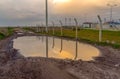 Puddle on earth road near wire netting at sunset Royalty Free Stock Photo