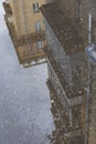 Puddle reflections of walls, windows, roofs of buildings and blue sky on wet asphalt pavement of city street road after summer