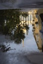 Puddle reflections of walls, windows, roofs of buildings and blue sky on wet asphalt pavement of city street road after summer