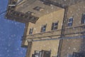 Puddle reflections of walls, windows, roofs of buildings and blue sky on wet asphalt pavement of city street road after summer