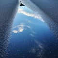 A puddle on a textured asphalt surface reflects a clear sky and fluffy clouds, creating Royalty Free Stock Photo