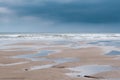 Puddles on a beach at low tide with low heavy grey clouds