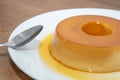 Pudim de leite, or pudding also known as flan on a wooden table with a metallic spoon