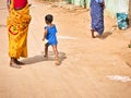 Small child with 2 women running on the street holding bag of chips in hand. Dalit boy, very poor indian