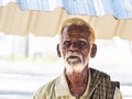 An unidentifed old senior indian poor man portrait with a dark brown wrinkled face and white hair and a white beard, looks serious