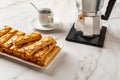 Puff pastries with an apricot glase on a white rectangular plate, cup of hot coffee and geyser coffee maker over marble surface. Royalty Free Stock Photo