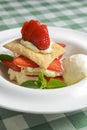 Puff pastries with strawberries and berry sauce on a white plate. Over green plaid background. Royalty Free Stock Photo