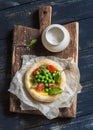 Puff pastry egg tartlet with fresh green peas and cherry tomatoes on wooden rustic board.
