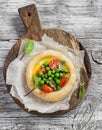 Puff pastry egg tartlet with fresh green peas and cherry tomatoes on wooden rustic board.