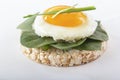 Puffed exploded wheat grains with fried egg and spinach leaves on a light wooden background.