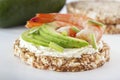 Puffed exploded wheat grains with shrimps and avocado slices on a thin layer of soft cheese on a light wooden table.