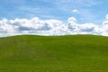 Puffy white clouds and blue sky over a huge beautiful idyllic vibrant green grassy field with gently rolling hills in the backgrou Royalty Free Stock Photo