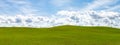 Puffy white clouds and blue sky over a huge beautiful idyllic vibrant green grassy field with gently rolling hills in the backgrou Royalty Free Stock Photo