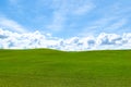 Puffy white clouds and blue sky over a huge beautiful idyllic vibrant green grassy field with gently rolling hills in the backgrou Royalty Free Stock Photo