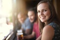 Pull up a chair. Portrait of a smiling young woman in a bar with some friends.