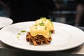 Pulled pork served on fried potato pancakes topped with poached egg and garnished with hollandaise sauce and fresh green onion aka Royalty Free Stock Photo