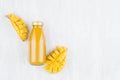 Pulpy fresh mango juice in glass bottle with gold cap, sliced fruit on white wood board, top view, copy space, mock up for design. Royalty Free Stock Photo