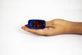 Pulse oximeter on finger used to test blood oxygen level in case of virus infection of the lungs with woman hand resting on white