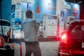 Pump boy completing filling petrol at an indian oil petrol pump in a waiting car with lights on closing the fuel cap while other