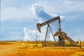 Pump jack oil gas well on red soil with storage tanks on horizon under dramatic sky Royalty Free Stock Photo