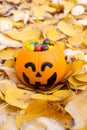 Pumpkin basket for Halloween, full of candy on the background of yellow fallen leaves, vertical frame