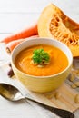 Pumpkin and carrot cream soup with pumpkin seeds and parsley in bowl on white wooden background. Royalty Free Stock Photo