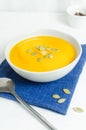 Pumpkin cream soup with seeds in a gray bowl and a metal spoon on a blue napkin on a white tablecloth. Royalty Free Stock Photo