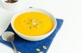 Pumpkin cream soup with seeds in a gray bowl and a metal spoon on a blue napkin on a white tablecloth. Royalty Free Stock Photo