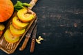 Pumpkin cut with slices on a wooden board. Fresh vegetables. On a black background. Free space for text. Royalty Free Stock Photo