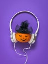 Pumpkin with a face in white headphones and a black hat on a purple background. Royalty Free Stock Photo