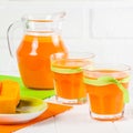 Pumpkin fresh juice in beautiful glasses and jug with pieces of ripe vegetable on white wooden background. Sweet orange juice. Hea Royalty Free Stock Photo