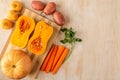 Pumpkin halves and a round small pumpkin on a bamboo cutting Board of two colors and other vegetables on a light wooden background