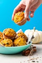 Pumpkin muffins with spices and seeds on plate. Women's hand takes muffin. Healthy sweet food. Blue background.