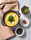 A pumpkin puree soup in a cast iron bowl with white cheese chunks and chopped parsley on top of a grey wooden table. Beige napkin Royalty Free Stock Photo