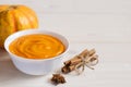 Pumpkin puree soup in a white bowl, fresh pumpkin, cinnamon sticks and star anise on a light wooden table Royalty Free Stock Photo