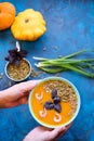 Pumpkin soup with green onions and prawns in women hands on a blue background. Top View