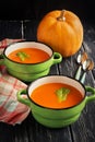 Pumpkin soup puree in ceramic small green saucepans on a wooden table.