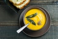 Pumpkin soup with sage leaves in brown ceramic soup plate with garlic bread.