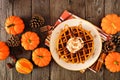 Fall breakfast pumpkin spice waffle with whipped topping, caramel and pecans. Top view table scene against dark wood.