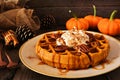 Autumn pumpkin spice waffle with whipped topping, caramel and pecans. Table scene against dark wood.