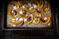 Pumpkin or squash slices with red onions, garlic, feta cheese and thyme on a baking tray in the oven, autumn vegetable meal for