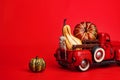 Pumpkins in red toy truck with human skeleton on red background. Happy Halloween. Space for text