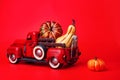 Pumpkins in red toy truck with human skeleton on red background. Happy Halloween. Space for text