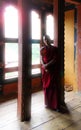 Punakha, Bhutan - September 10, 2016: Young novice Buddhist monk in reddish robe standing in front of a window inside a monastery. Royalty Free Stock Photo