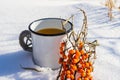 Punch with sea buckthorn berries in an iron white mug in the snow. Sea buckthorn twigs with tea