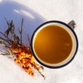 Punch with sea buckthorn berries in an iron white mug in the snow. Sea buckthorn twigs with tea