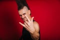 Punk with black electric guitar, mustache and big mohawk showing horn gesture. Photo of a rock musician in the studio on a red Royalty Free Stock Photo