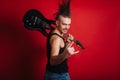 Punk with black electric guitar, mustache and big mohawk showing horn gesture. Photo of a rock musician in the studio on a red Royalty Free Stock Photo